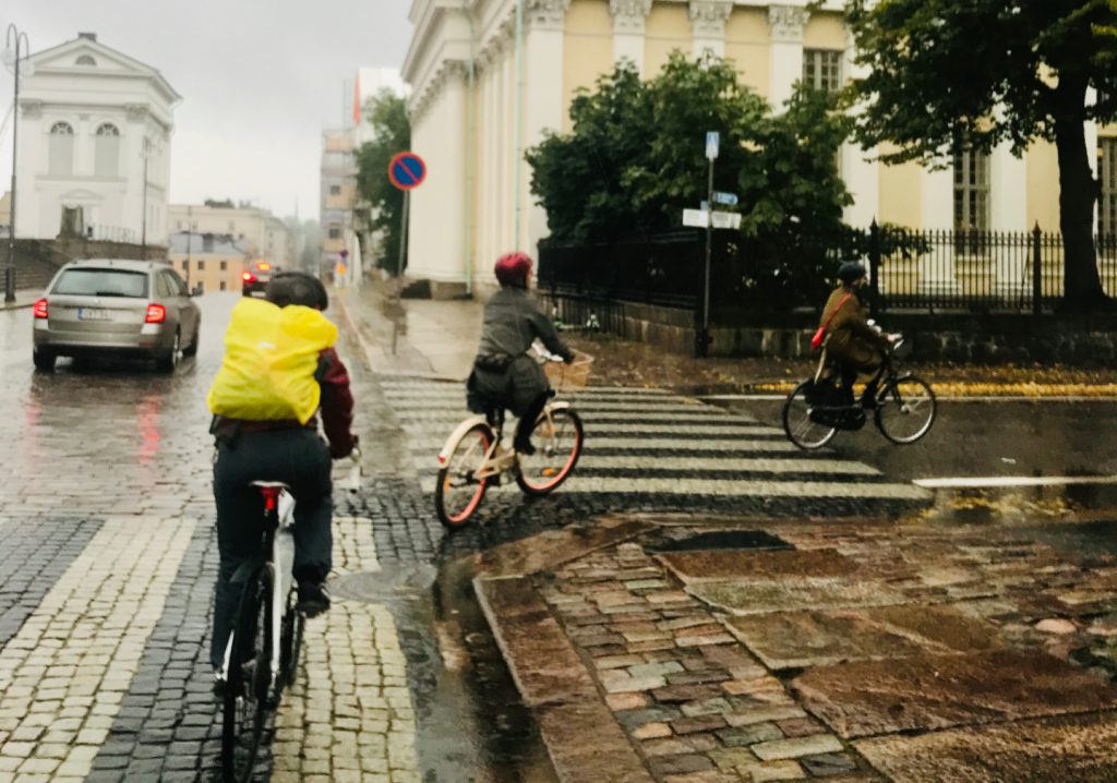 kolme pyöräilijää ja auto Helsingin kaduilla